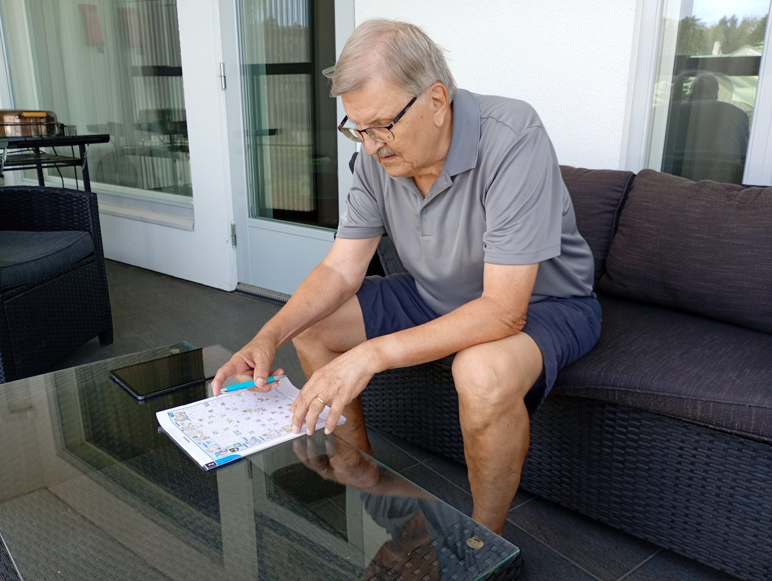 Mies istumassa sohvalla, tekemässä ristisanatehtävää.